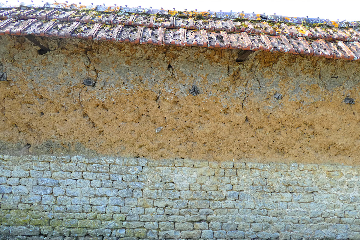 Mur d’enceinte relictuel d’une ferme toujours en activité dans le Cotentin, au nord-ouest de la Manche (torchis et pierre de pays). 